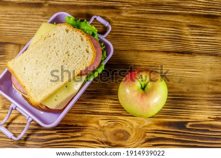 Lunch box with sandwiches and apple on a wooden table. Top view