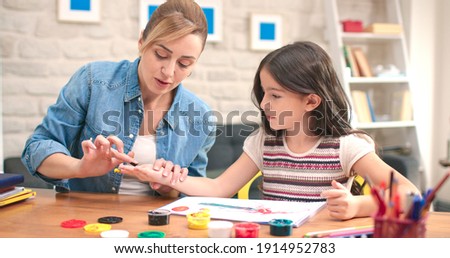 At the desk, the girl and her mother paint with their fingers. Happy family. The concept of having a good time with their children.