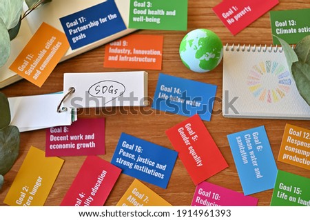 There is a word book with SDGs written on it and a sketchbook with symbols drawn on it. On that desk, there are cards with SDGs goals scattered around, by the ball of the earth. Royalty-Free Stock Photo #1914961393