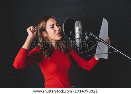 Pretty Asian female singer recording songs by using a studio microphone and pop shield on mic with passion in music recording studio. Performance and show in the music business. Image with copy space.