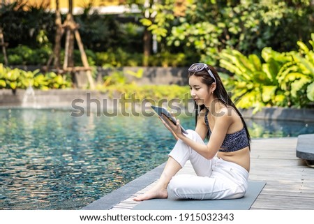 Beautiful asian woman relaxing with using digital tablet computer outdoors by the swimming pool