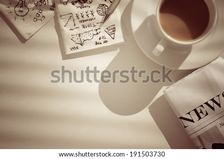 Coffee, newspaper and napkins with pictures, showing business breakfast