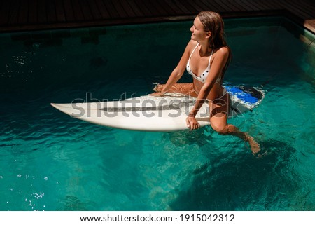 Happy young  woman in bikini is sunbathing on a surfboard in pool