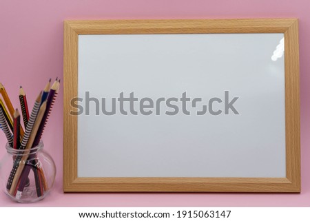 A blank white wooden picture frame with pink background and pencils