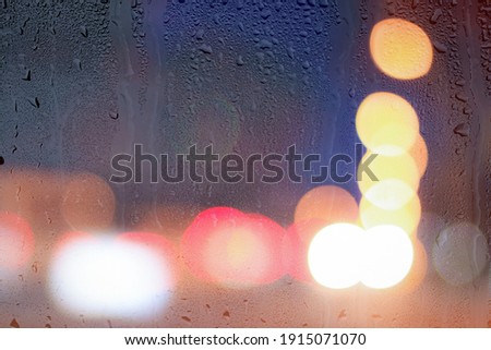 Night city lights and car headlights through rainy glass. Rain and bad wet weather concept.