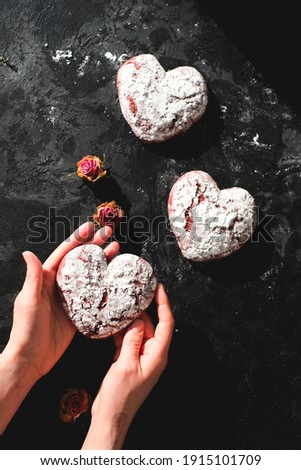Tasty heart shape form cookies on background table. Homemade red cookie with sugar icing. St.Valentine sweets. Woman hands. Close up view delicious sweet dessert