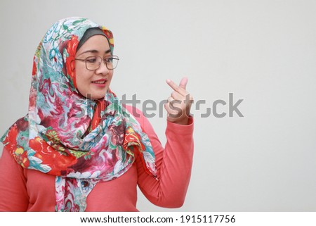 Smiling Asian Muslim lady makes Korean love sign, finger heart gesture, I Love You.