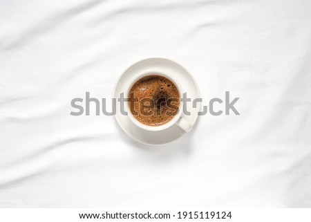 top view of hot coffee in white ceramic cup on white ceramic plate placed on blank clean tablecloths with soft light in the morning. Royalty-Free Stock Photo #1915119124