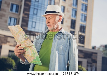 Photo of attractive confident mature man wear jeans shirt headwear walking looking map outside urban city street