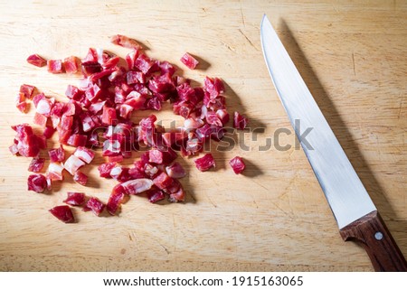Iberian ham (serrano) cut into cubes (diced). On wooden board with knife.