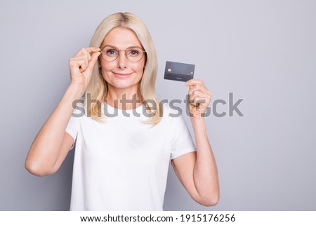 Photo portrait of old lady holding credit card in one hand isolated on grey colored background