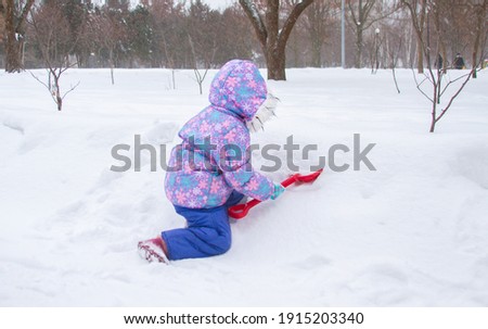 Little girl playing with snow, child dripping snow with a shovel, children's winter games.
