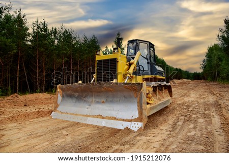 Dozer during clearing forest for construction new road. Bulldozer at forestry work on sunset background. Earth-moving equipment at road work, land clearing, grading, pool excavation, utility trenching Royalty-Free Stock Photo #1915212076