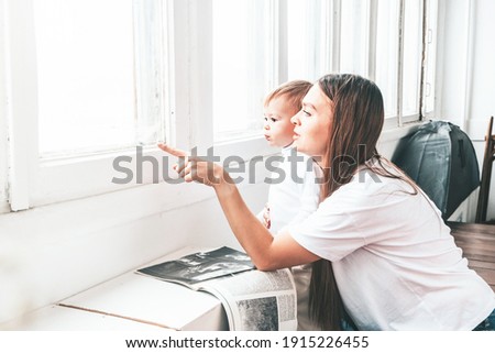 Beautiful young woman with a small child are sitting near the window. Mom and daughter are leafing through the magazine. Light cozy interior. Mother's day picture