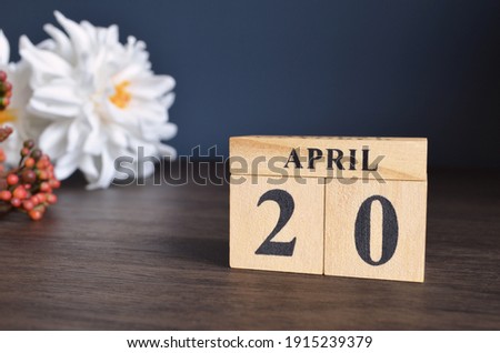 April 20, Date cover design with calendar cube and white Paeonia flower on wooden table and blue background.