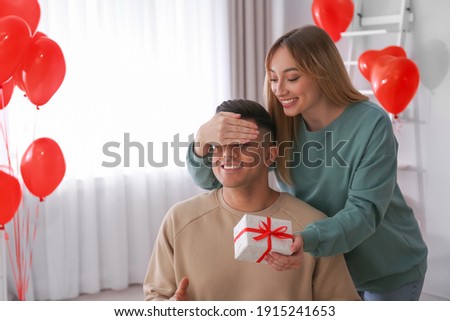 Woman presenting gift to her boyfriend in room decorated with heart shaped balloons. Valentine's day celebration