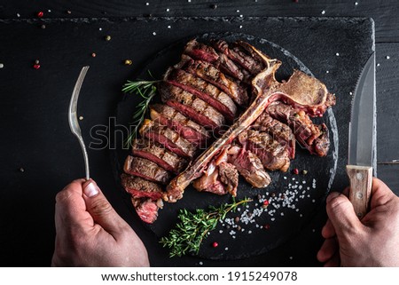 Dry Aged Barbecue Porterhouse Steak. Succulent grilled large t-bone steak garnished with fork and knife. American meat restaurant. banner, catering menu recipe place for text. Royalty-Free Stock Photo #1915249078