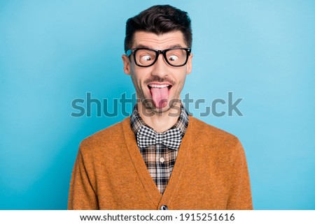 Photo of crazy funny young nerdy man stick tongue out fooling face joke isolated on blue color background