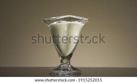 Close up of pouring milk or yogurt into the transparent glass isolated on beige wall background. Stock footage. Concept of calcium and healthy breakfast.