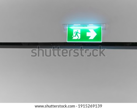 White Illuminated Fire Exit Sign on Green Panel Under Ceiling