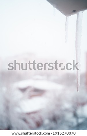vertical view of macro detail of a water frozen stalactite in the window at home. Winter background with white copyspace.