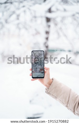 vertical view of unrecognizable woman holding a smartphone taking a picture in the snowy countryside. Technology and winter concept. Screen photo of a Christmas landscape with copyspace.