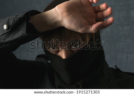 A young guy with brown eyes in a balaclava poses in front of the camera on a dark background