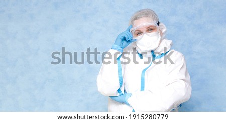 Medical worker in a white protective suit on a blue background. Wear a respirator and gloves. Place for an inscription. Panorama.
