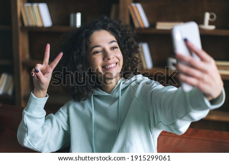 Happy african american woman take selfie picture at modern smartphone, showing victory sign on camera, using online app. Social influencer or blogger talking with subscribers and followers