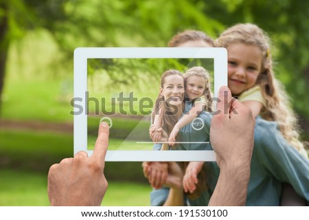Hand holding tablet pc showing mother giving daughter a piggy back