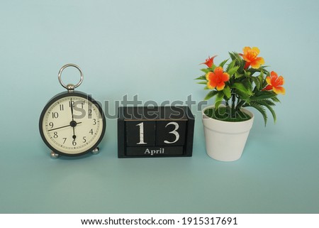alarm clock with cube date and flower on the blue background. April 13 concept.