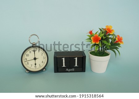alarm clock with cube date and flower on the blue background. April 11 concept.
