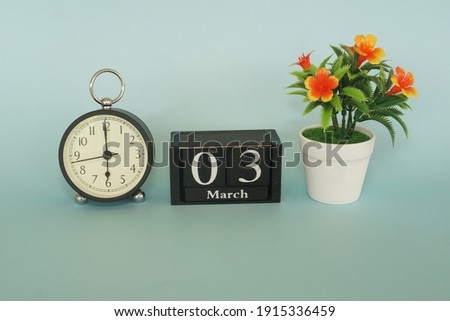 alarm clock with cube date and flower on the blue background. March 3 concept.