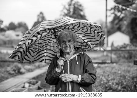 An old woman outdoors standing under a umbrella. Black and white photo.