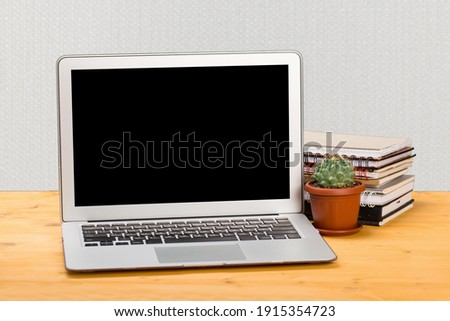Laptop with blank screen, place for text and notebooks and green cactus on a wooden table.