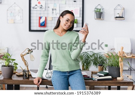 happy african american architect smiling at camera while messaging on smartphone