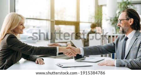 Confident business partners is shaking hands at meeting or after successful negotiations, sitting in modern office. Influential employees sign an important contract or deal, collaboration concept Royalty-Free Stock Photo #1915384786