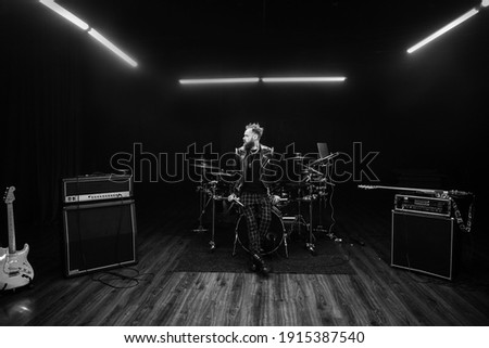 brutal portrait of a man musician with a beard and in black clothes on the background of musical instruments drums