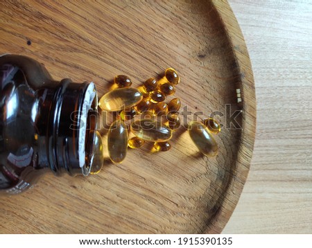 gelled transparent oil vitamin capsules scattered from brown glass bottle on wooden plate 