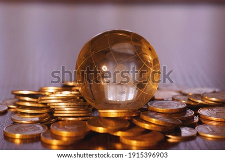 A small glass globe with coins on a colored background.