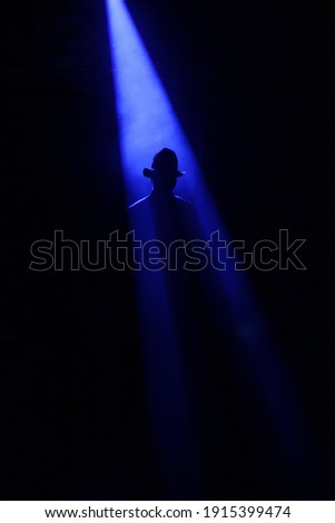 silhouette of a man in a hat on the background of a ray of light in a black room