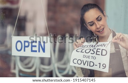 As Covid-19 restrictions ease, restaurant owner unsticks the closure sign putting open sign on a window.