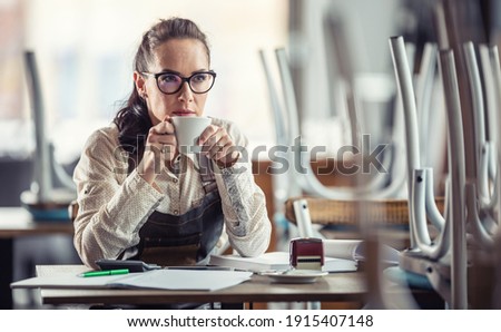 Business owner sips coffee sitting over accounting of her closed bar or restaurant.
