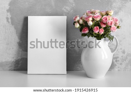 Blank canvas and pink flowers on table. White stretched canvas for mock up