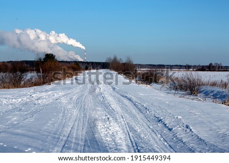 
Snowy road in the forest. Against the background of smoking industrial chimneys