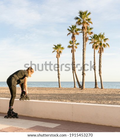 Fitness female tying the laces of roller skates before training outdoors.Active sports lifestyle concept, on beach with palm trees background with copy space.