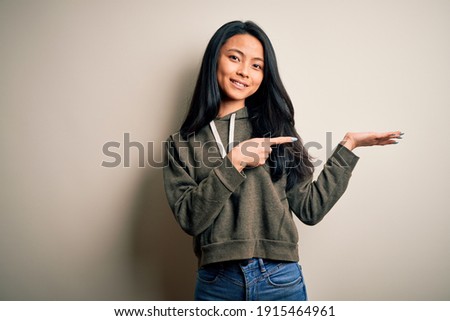 Young beautiful chinese sporty woman wearing sweatshirt over isolated white background amazed and smiling to the camera while presenting with hand and pointing with finger.