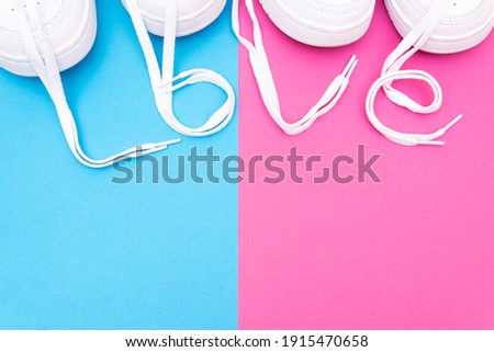 Two pairs of matching white sneakers with the lettering "love" made of the laces on a contrast pink blue background. Matching shoes for couples idea.