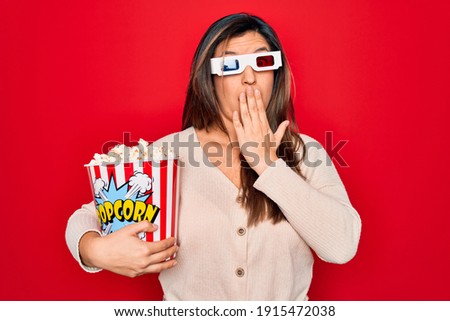 Young hispanic woman wearing 3d movie glasses and eating popcorn over red background cover mouth with hand shocked with shame for mistake, expression of fear, scared in silence, secret concept