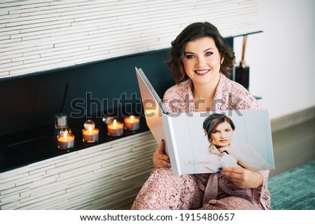Young happy woamn looking at photo album, resting in cozy living room